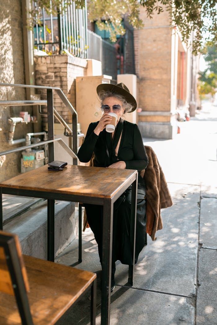Elegant senior woman with a hat enjoying coffee at an outdoor cafe on a sunny day.