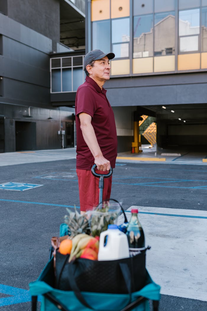 Elderly man with a grocery cart in an outdoor parking lot, wearing a maroon shirt.