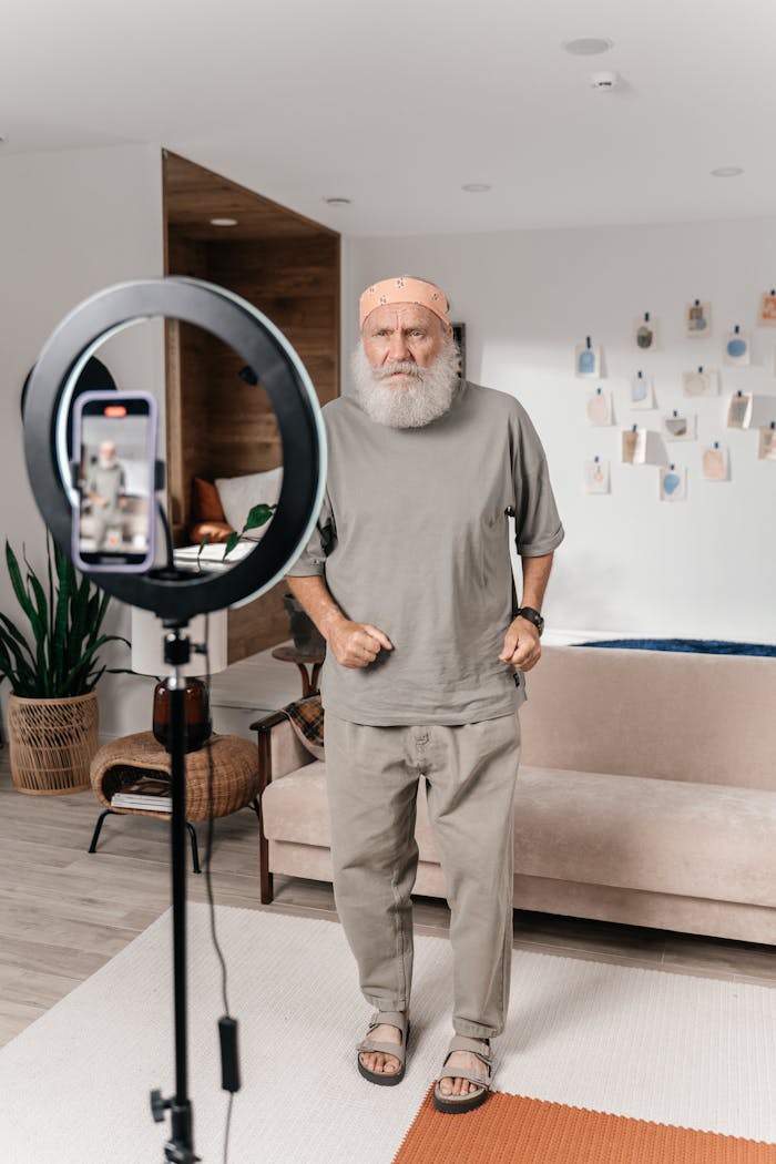 Elderly man creating social media content at home with smartphone and ring light.